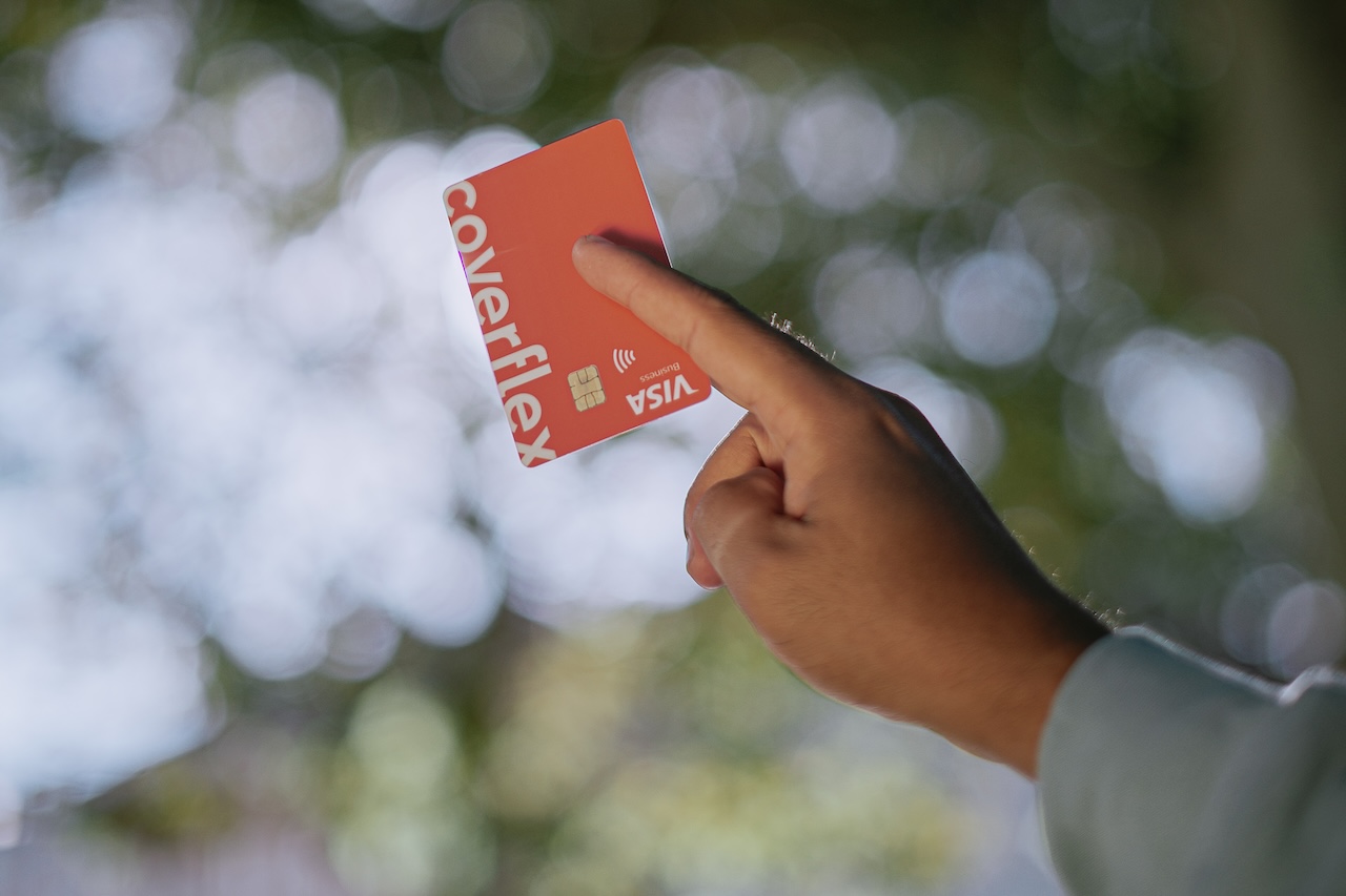 L'immagine mostra una persona sorridente che utilizza un'app Coverflex su uno smartphone. Lo schermo dell'app visualizza un saldo e opzioni per benefit aziendali, suggerendo un'interfaccia utente intuitiva per la gestione dei vantaggi per i dipendenti.