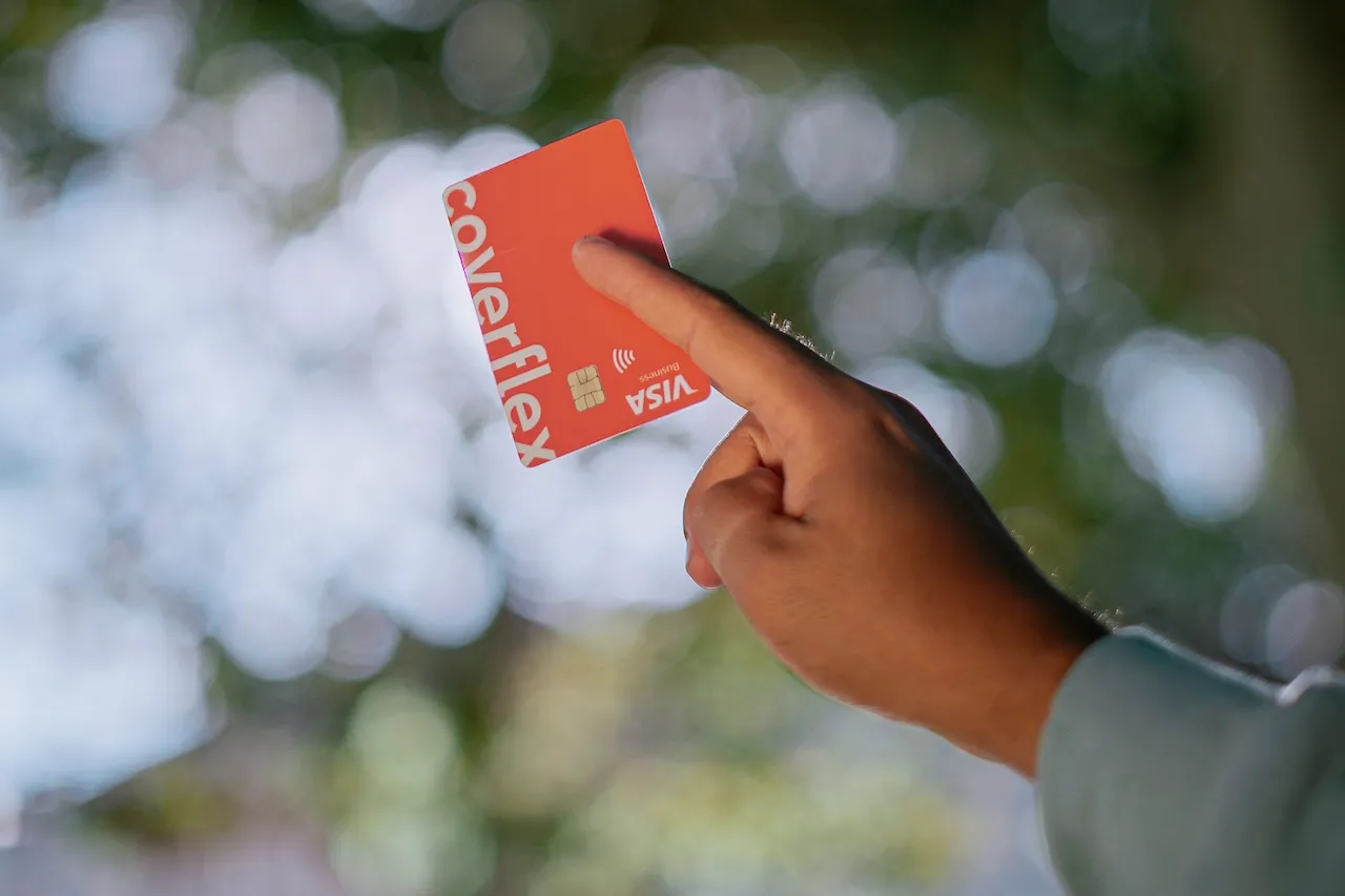 L'immagine mostra una persona sorridente che utilizza un'app Coverflex su uno smartphone. Lo schermo dell'app visualizza un saldo e opzioni per benefit aziendali, suggerendo un'interfaccia utente intuitiva per la gestione dei vantaggi per i dipendenti.