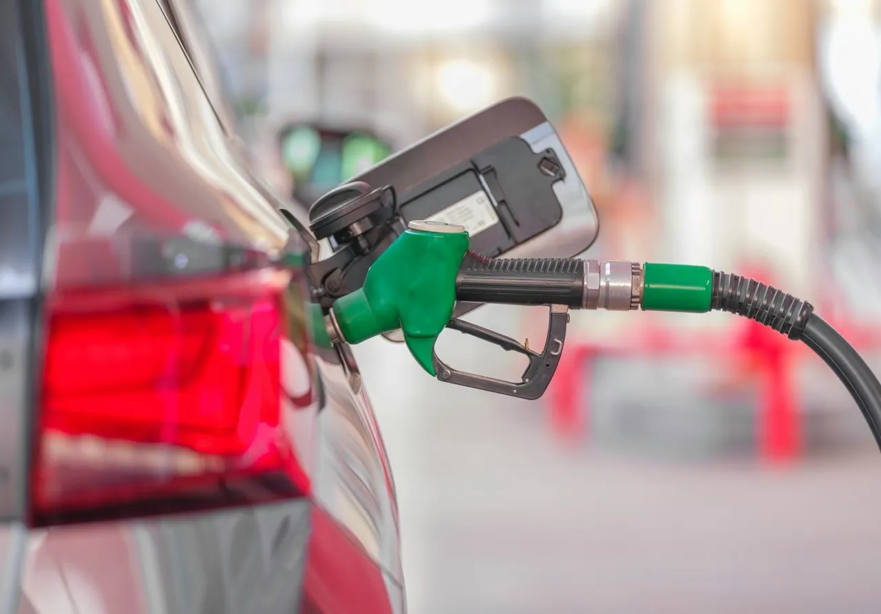 Primo piano di una pistola erogatrice verde collegata al bocchettone del carburante di un veicolo rosso in una stazione di servizio