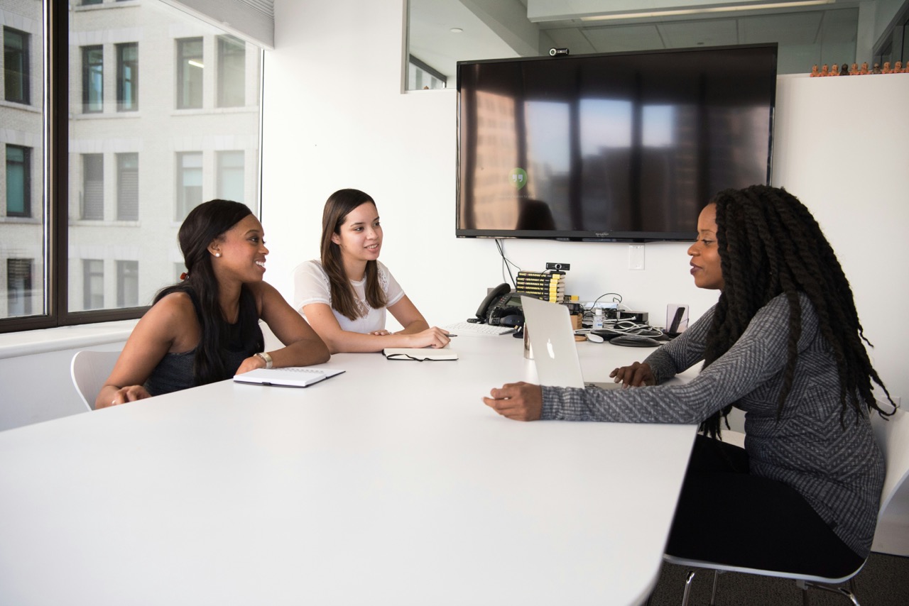 Tre donne professioniste di etnie diverse sorridono durante un colloquio in una sala riunioni moderna