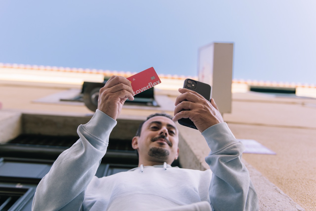 inquadratura dal basso di un uomo mentre aggiunge la carta coverflex rossa a google pay sullo smartphone davanti a una facciata urbana