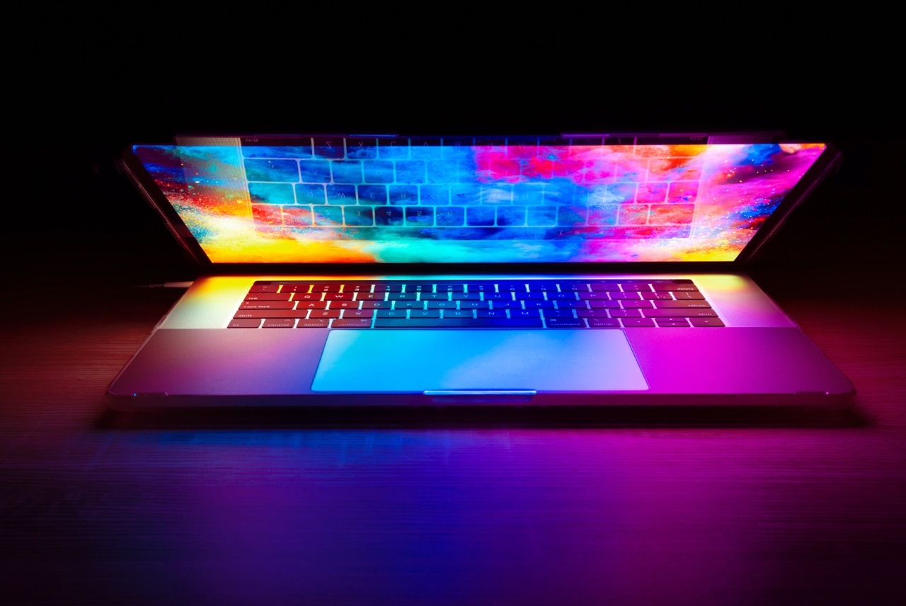 Laptop aperto con schermo luminoso dai colori vividi che proietta riflessi arcobaleno sulla tastiera e sul piano di lavoro scuro