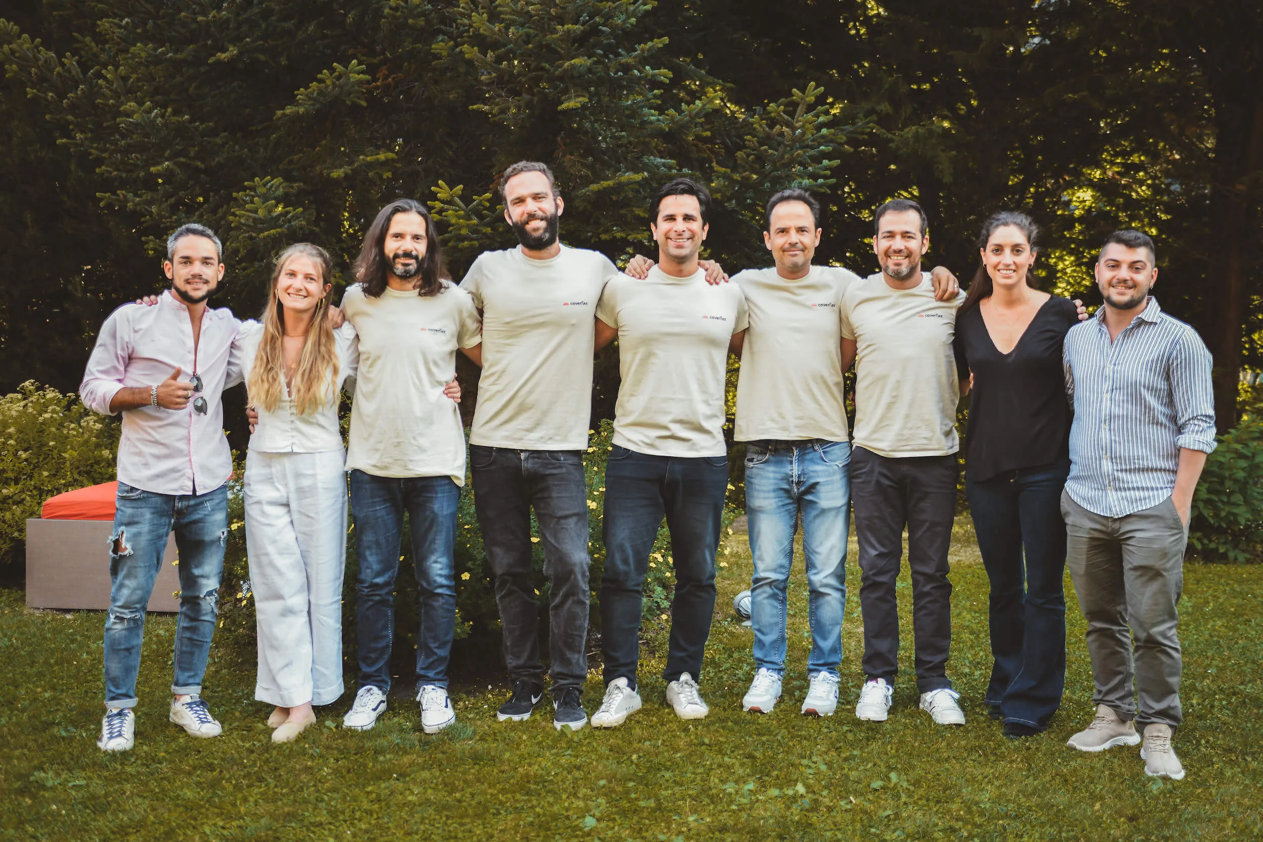 Nove membri del team di Coverflex ed EatsReady in abbigliamento casual e magliette brandizzate in piedi su un prato con alberi sullo sfondo mentre posano sorridenti