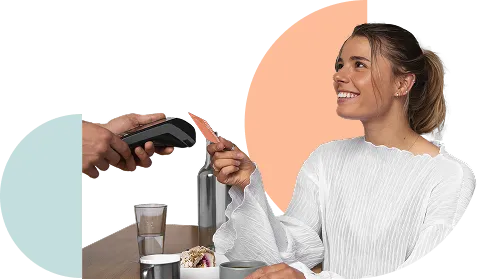 Smiling woman holding a credit card to pay at a restaurant table with a glass of water and a dessert.
