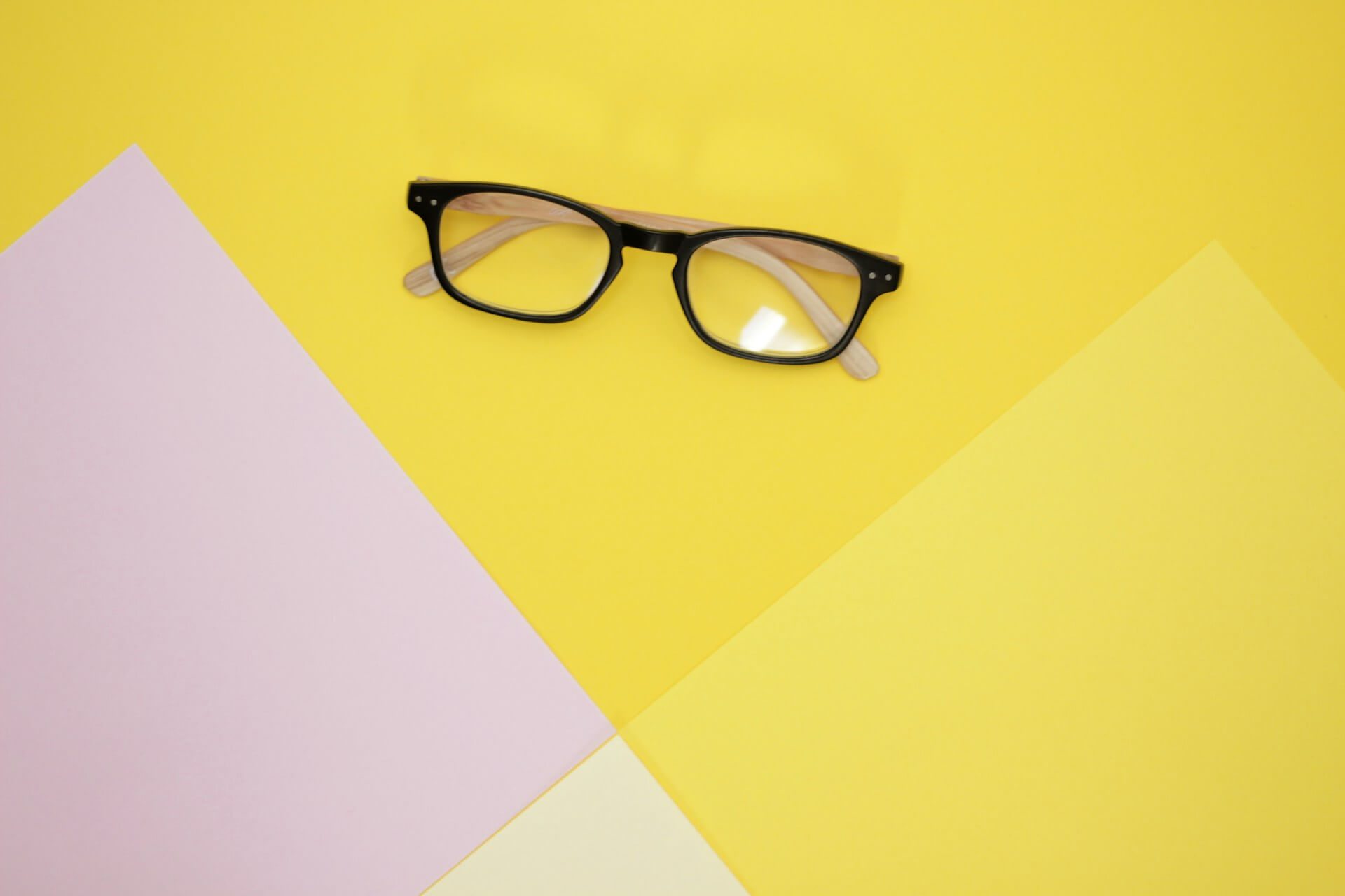Óculos de aro preto com hastes de madeira sobre fundo amarelo e rosa