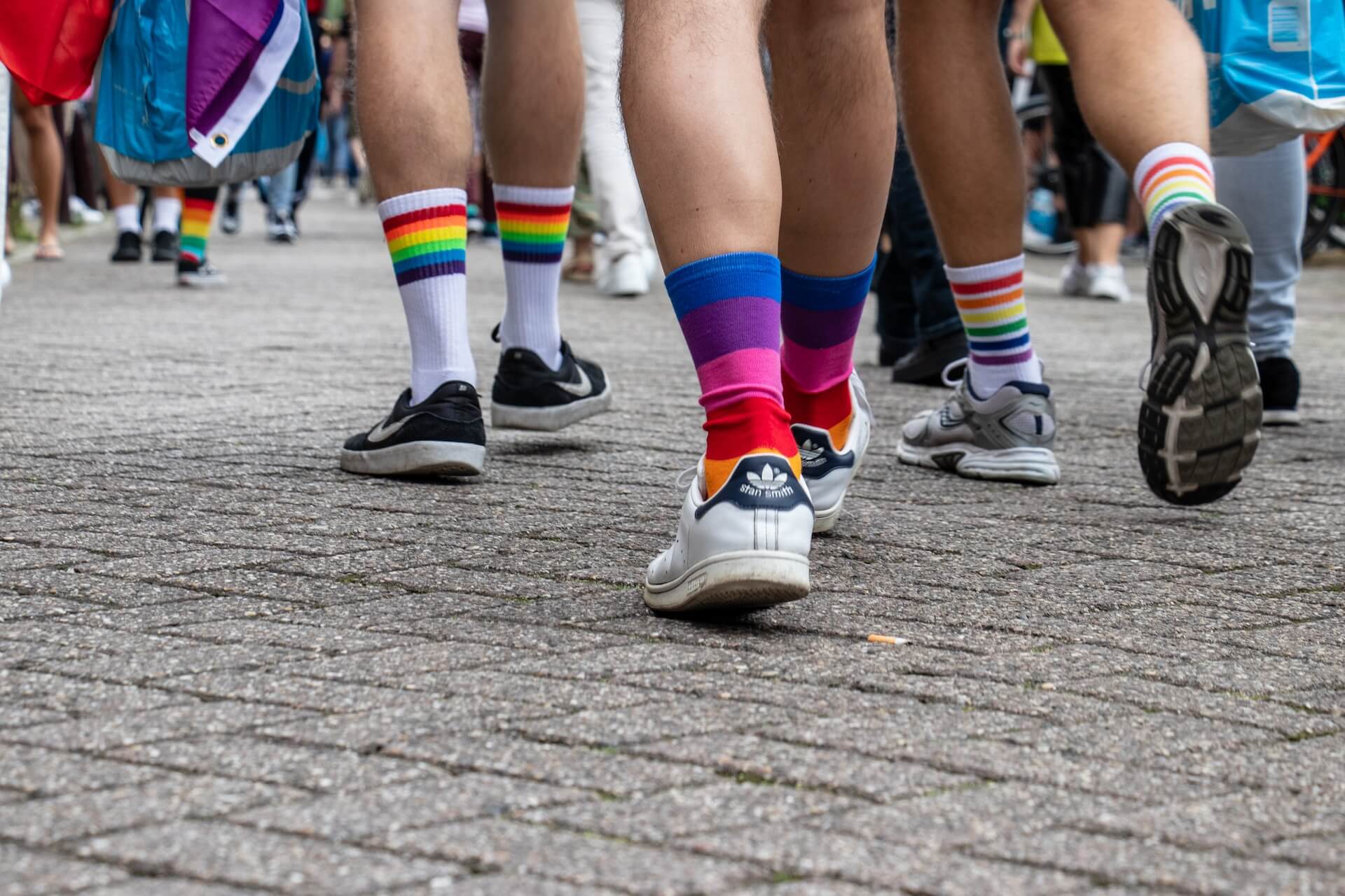 vista de pormenor de pés com meias arco-íris e sapatilhas a caminhar por calçada durante marcha do orgulho LGBT