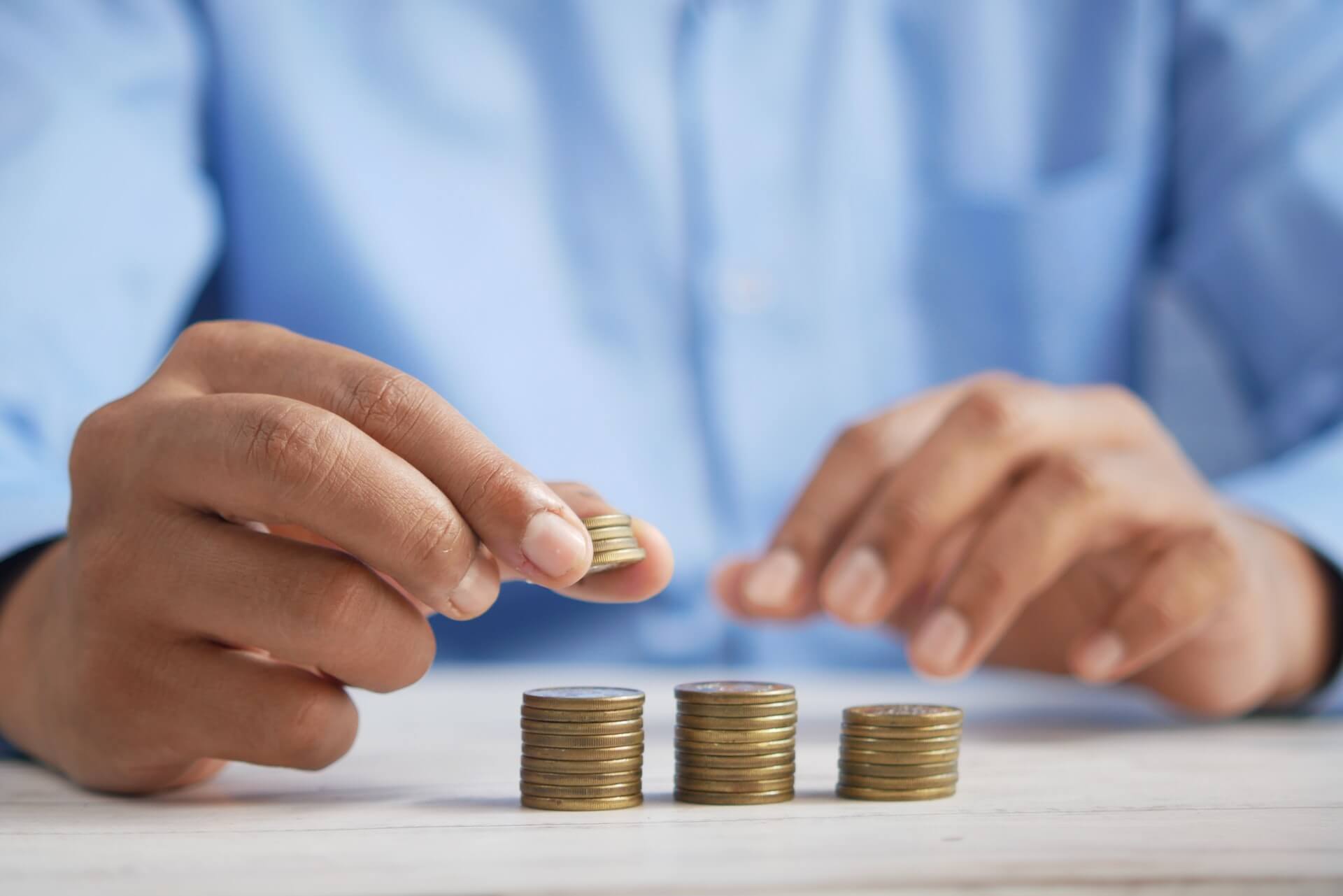 Close-up de mãos a organizar e empilhar moedas em três colunas sobre uma mesa, representando gestão financeira e poupança