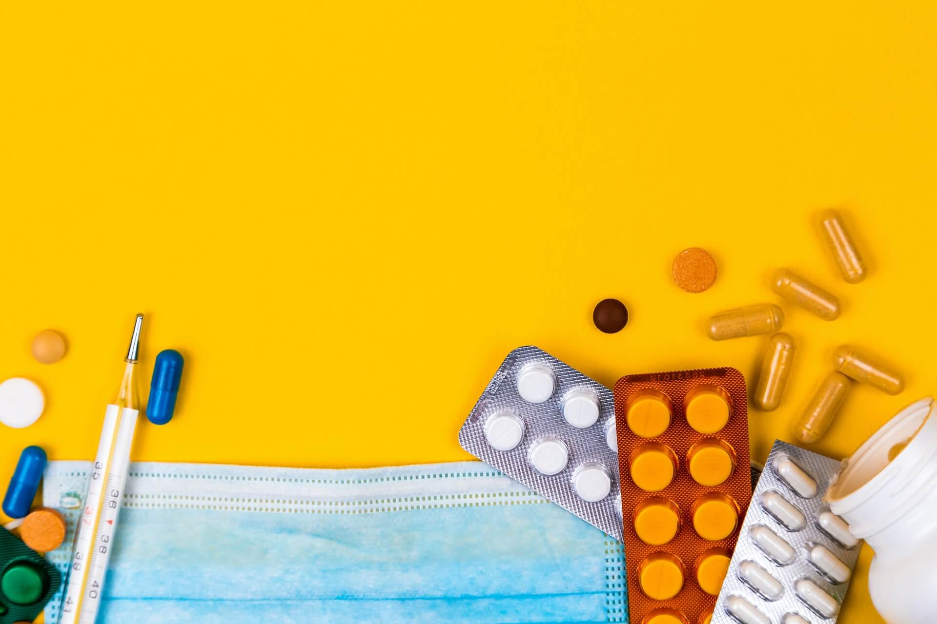 Imagem promocional da parceria entre Grupo Sofarma e Coverflex com máscara cirúrgica, termómetro e blisteres de comprimidos e cápsulas dispersos sobre fundo amarelo