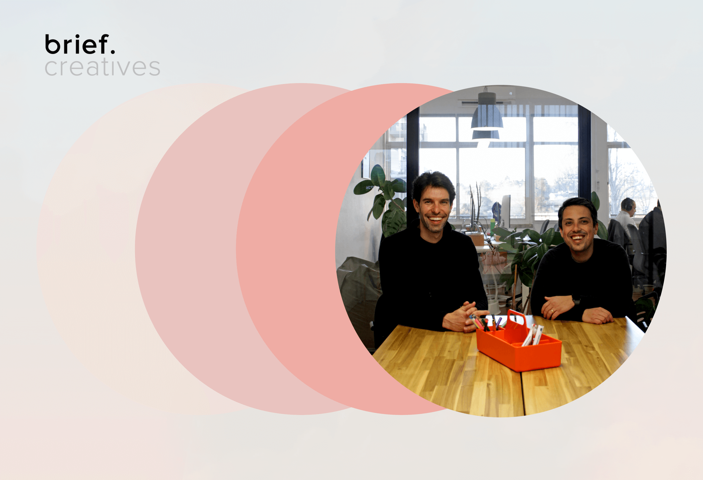 Dois cofundadores da Brief Creatives sorridentes sentados à mesa de madeira num escritório moderno, com caixa de canetas vermelha e logo da agência rodeados por círculos coloridos em sobreposição