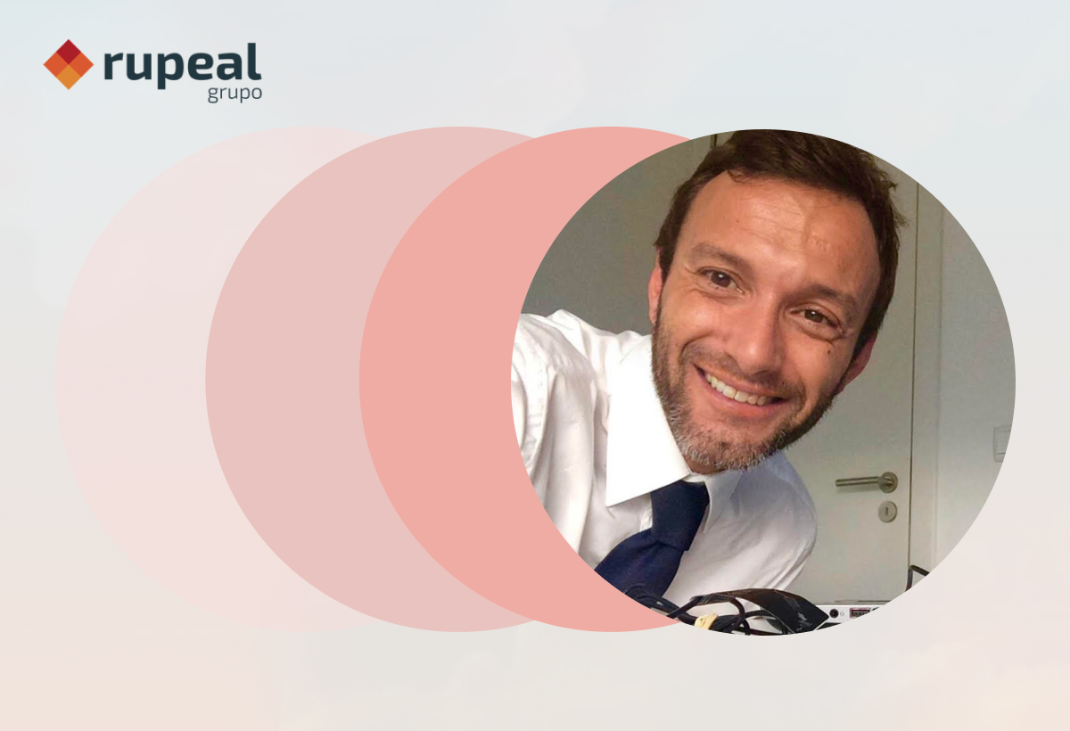 Logotipo rupeal grupo com rosto de colaborador sorridente de camisa e gravata num círculo sobreposto a esferas semitransparentes