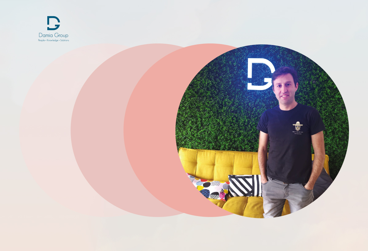 Colaborador Damia Group de pé junto a sofá amarelo e almofadas, em frente a parede verde com logotipo iluminado