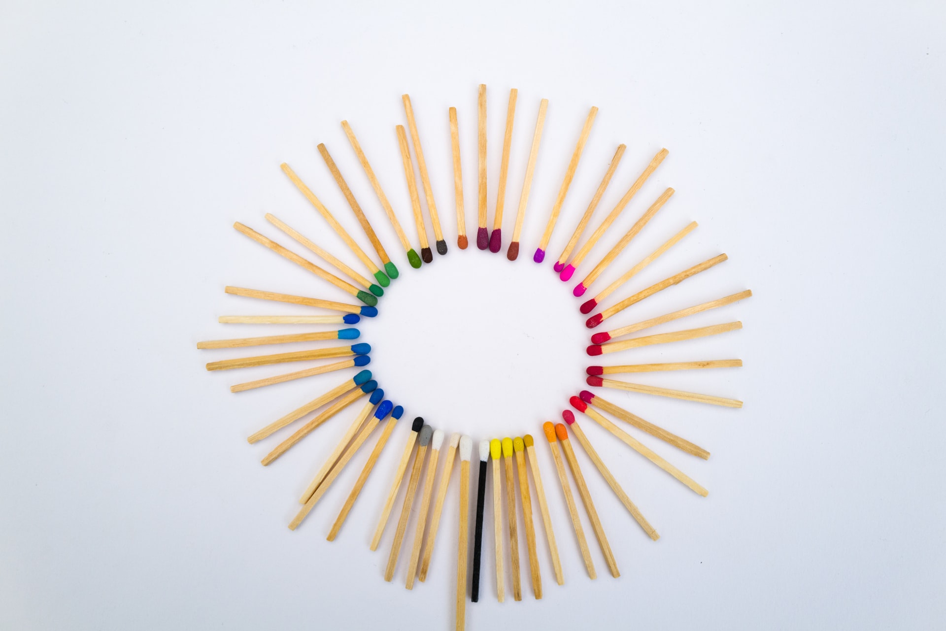Palitos de fosforo com pontas de cores variadas dispostos em circulo sobre fundo branco