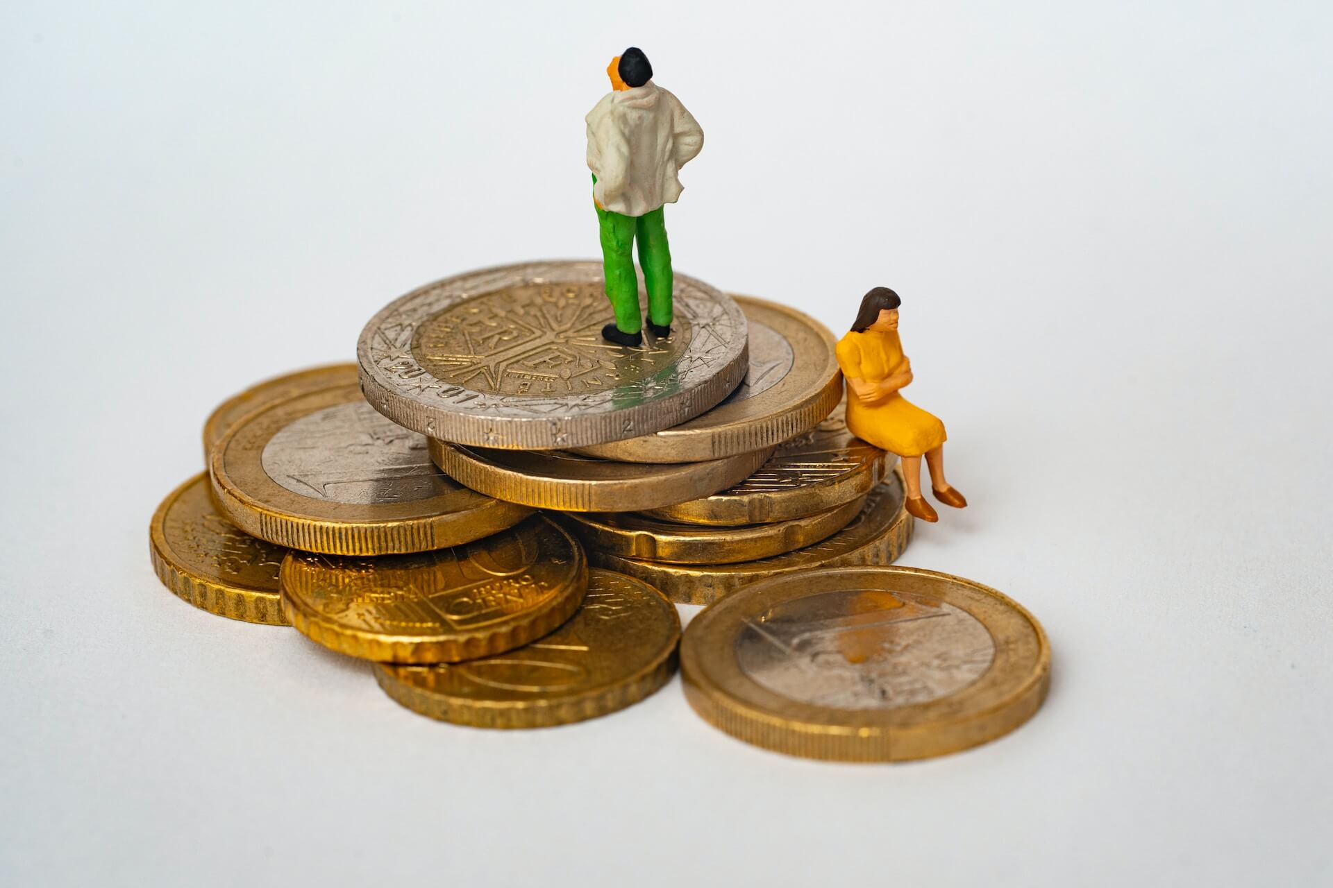 close-up of small man and woman models on euro coin pile symbolizing budgeting challenges and financial planning