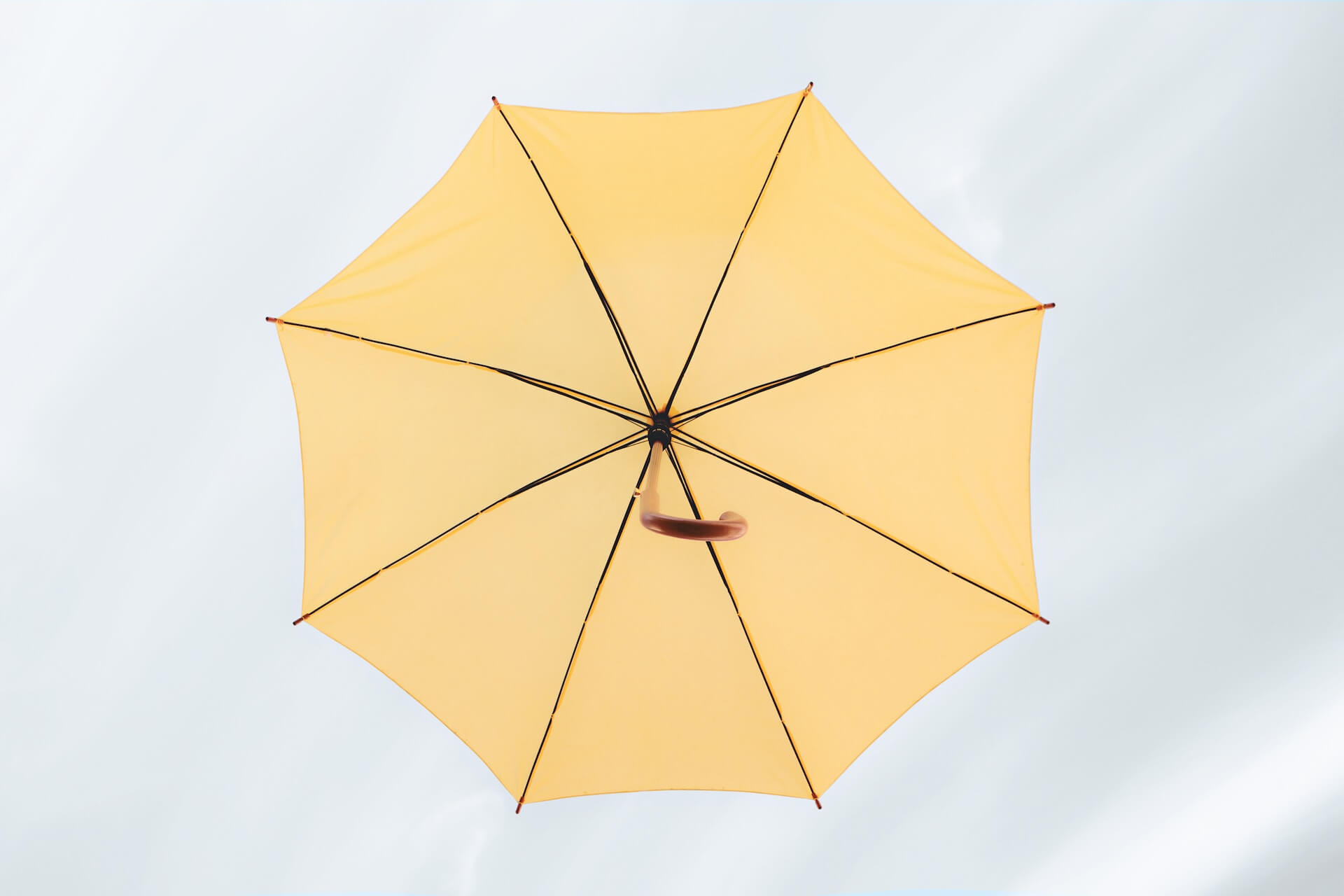 Open yellow umbrella viewed from below against a soft pale background