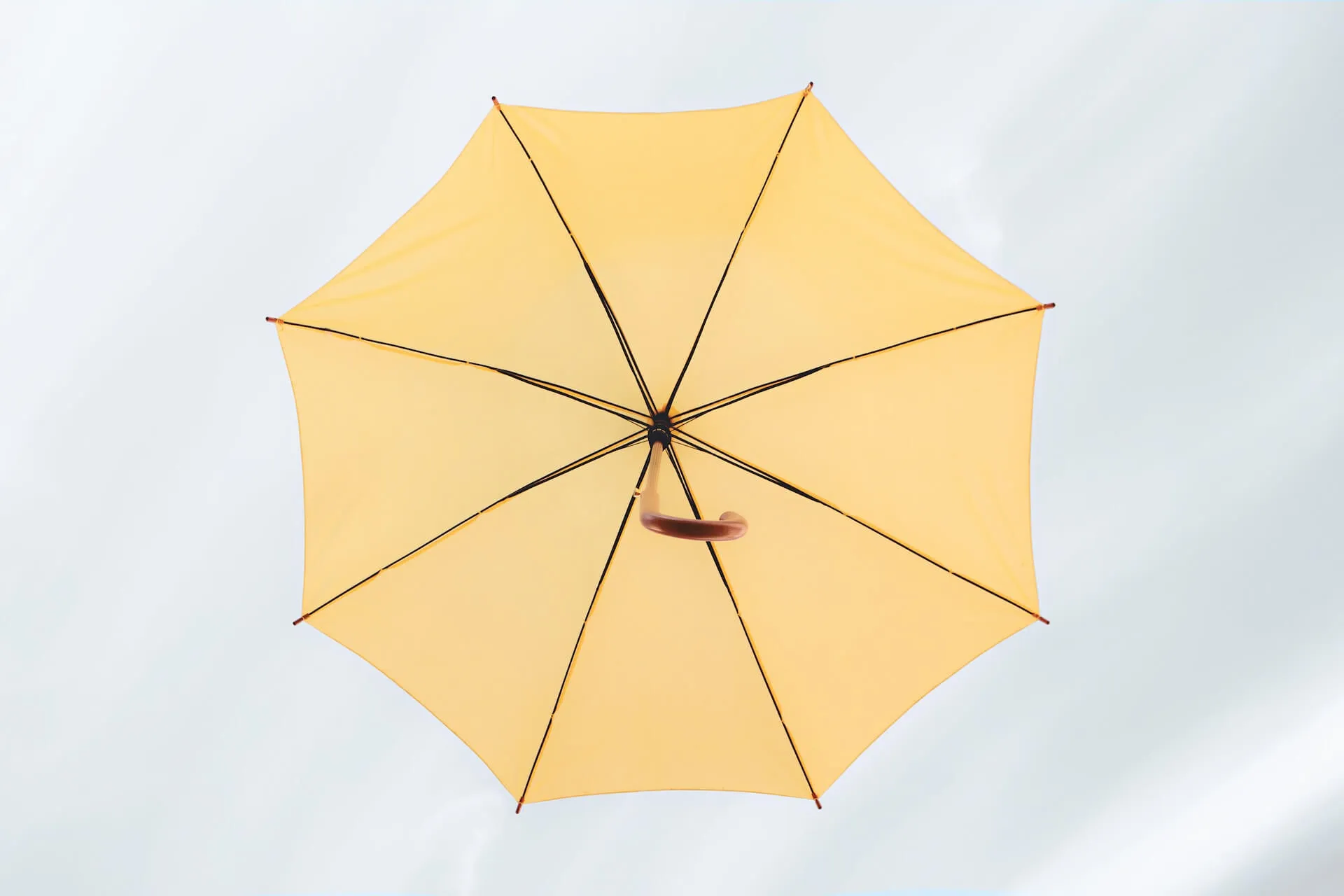 Open yellow umbrella viewed from below against a soft pale background