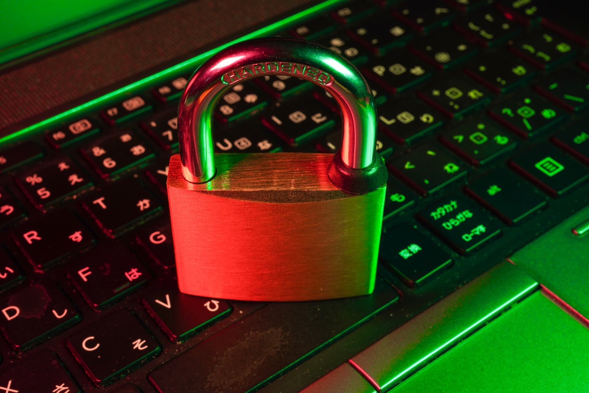 closeup of a brass padlock placed on a backlit laptop keyboard illuminated by red and green light symbolizing information security
