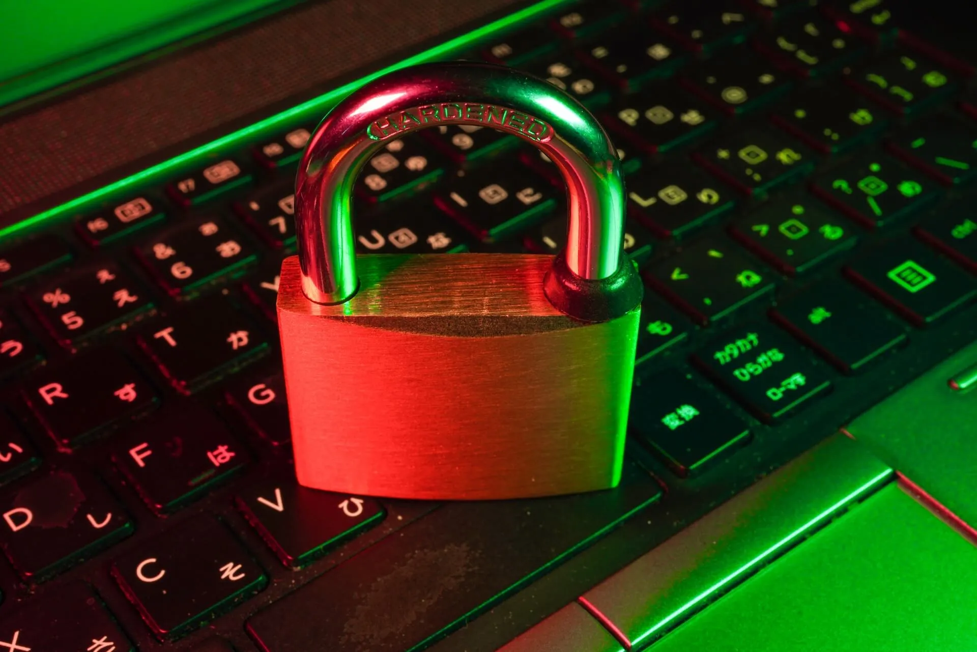 closeup of a brass padlock placed on a backlit laptop keyboard illuminated by red and green light symbolizing information security