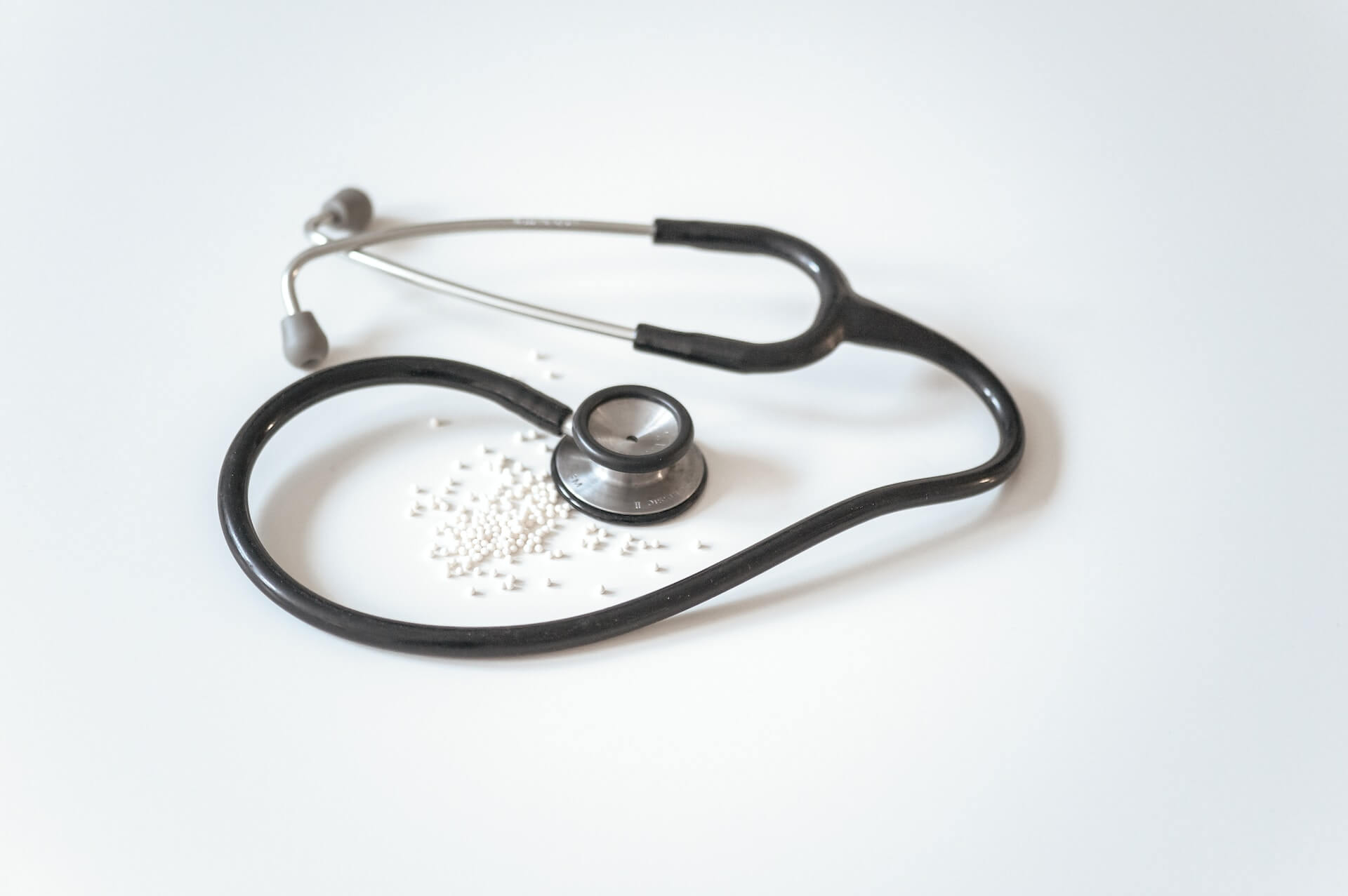 Close-up of a black stethoscope and scattered white pills on a plain background symbolising medical coverage