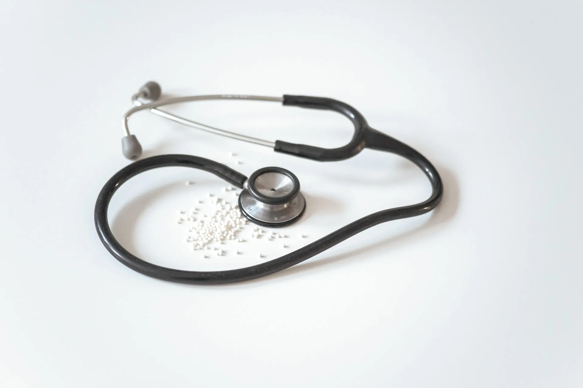Close-up of a black stethoscope and scattered white pills on a plain background symbolising medical coverage