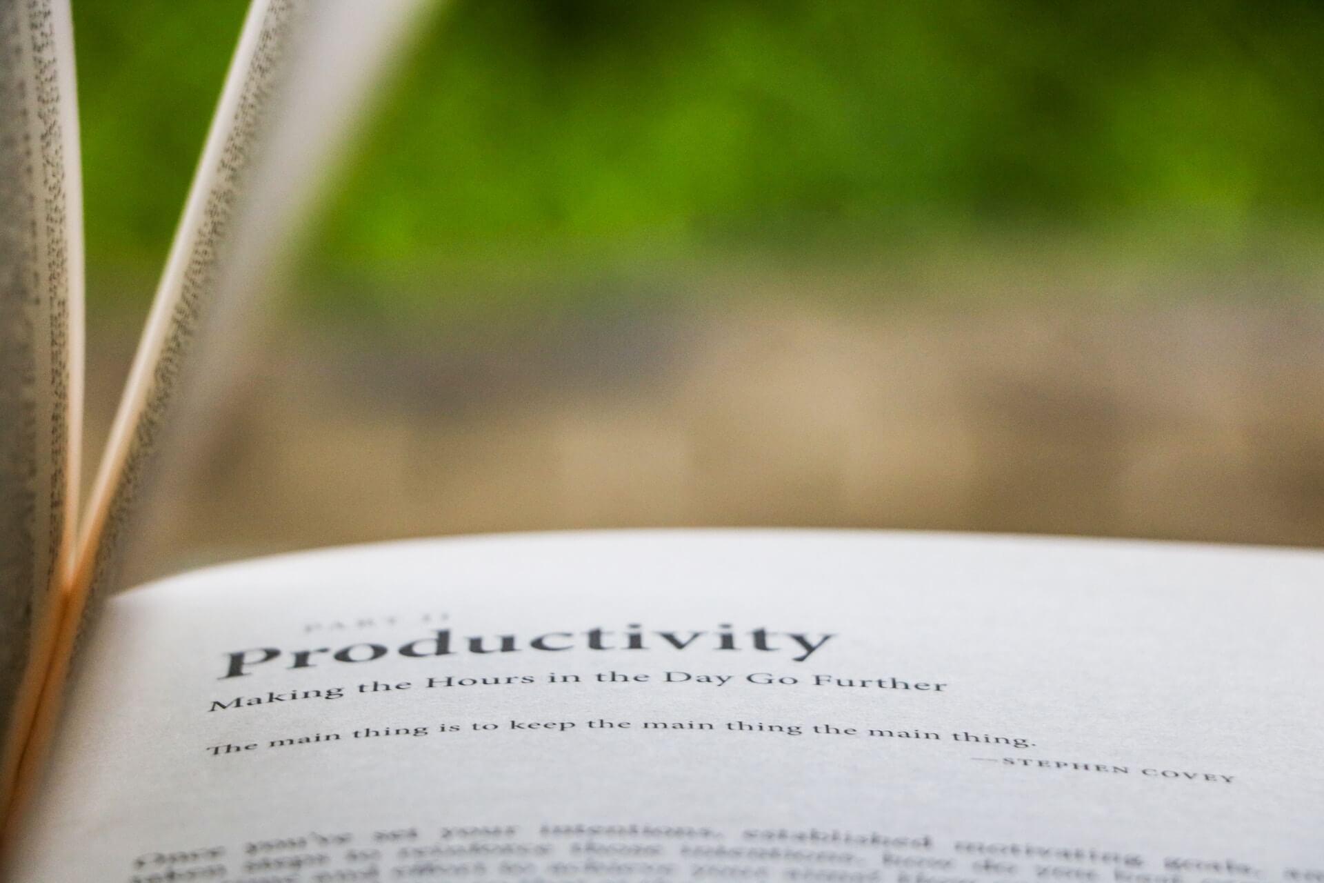 Close up of an open book showing the heading Productivity Making the Hours Go Further and the quote The main thing is to keep the main thing the main thing by Stephen Covey against a blurred green background