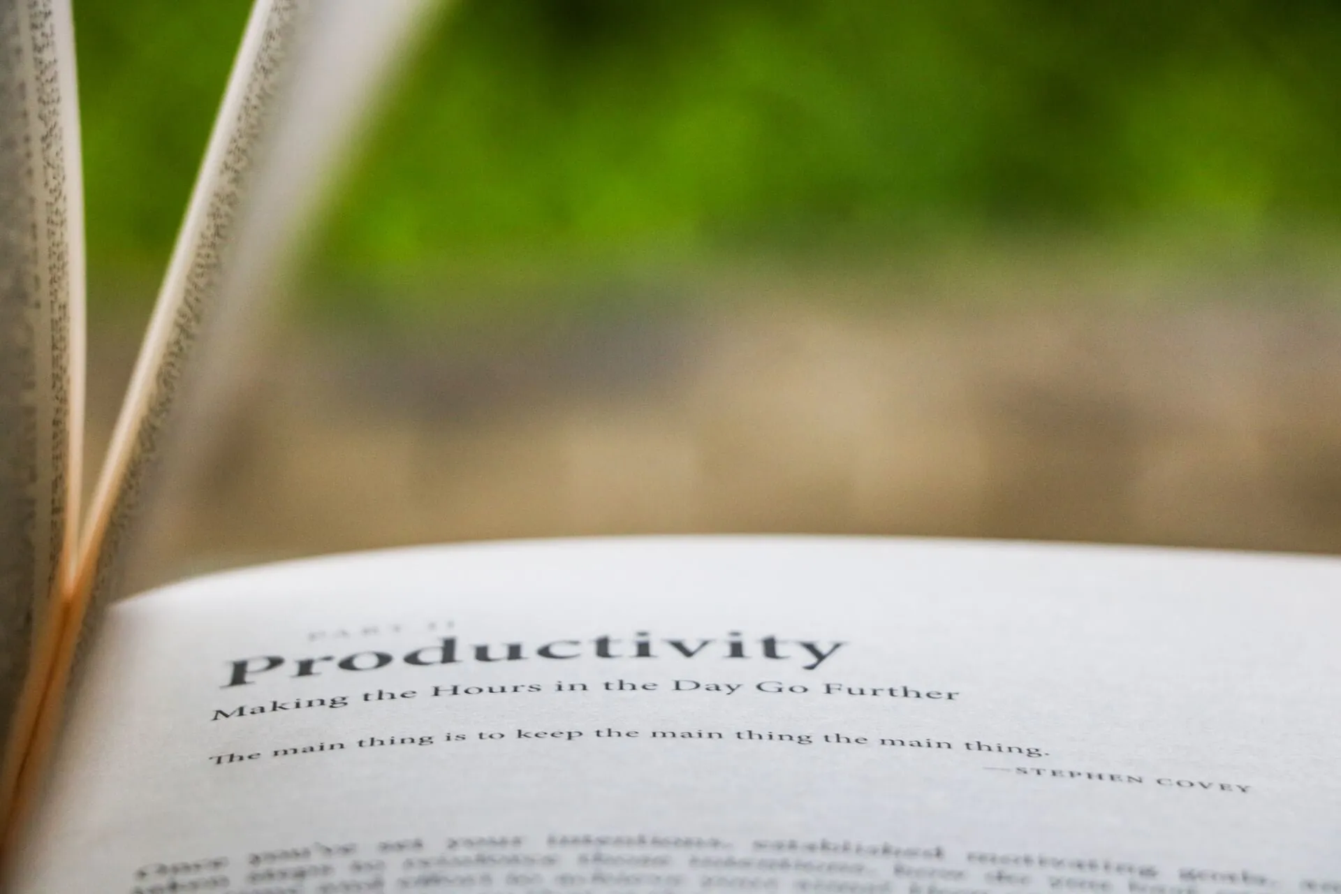 Close up of an open book showing the heading Productivity Making the Hours Go Further and the quote The main thing is to keep the main thing the main thing by Stephen Covey against a blurred green background