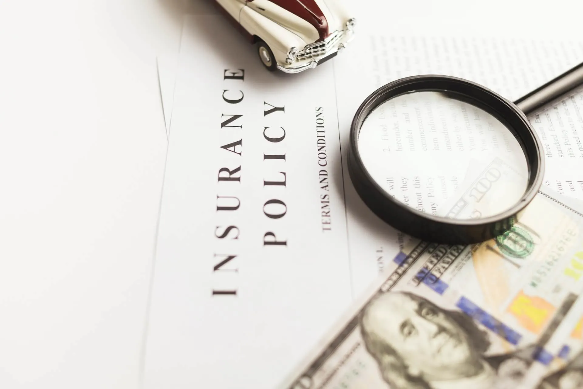 close up of insurance policy document with terms and conditions title a magnifying glass highlighting text beside a small model car and US currency notes