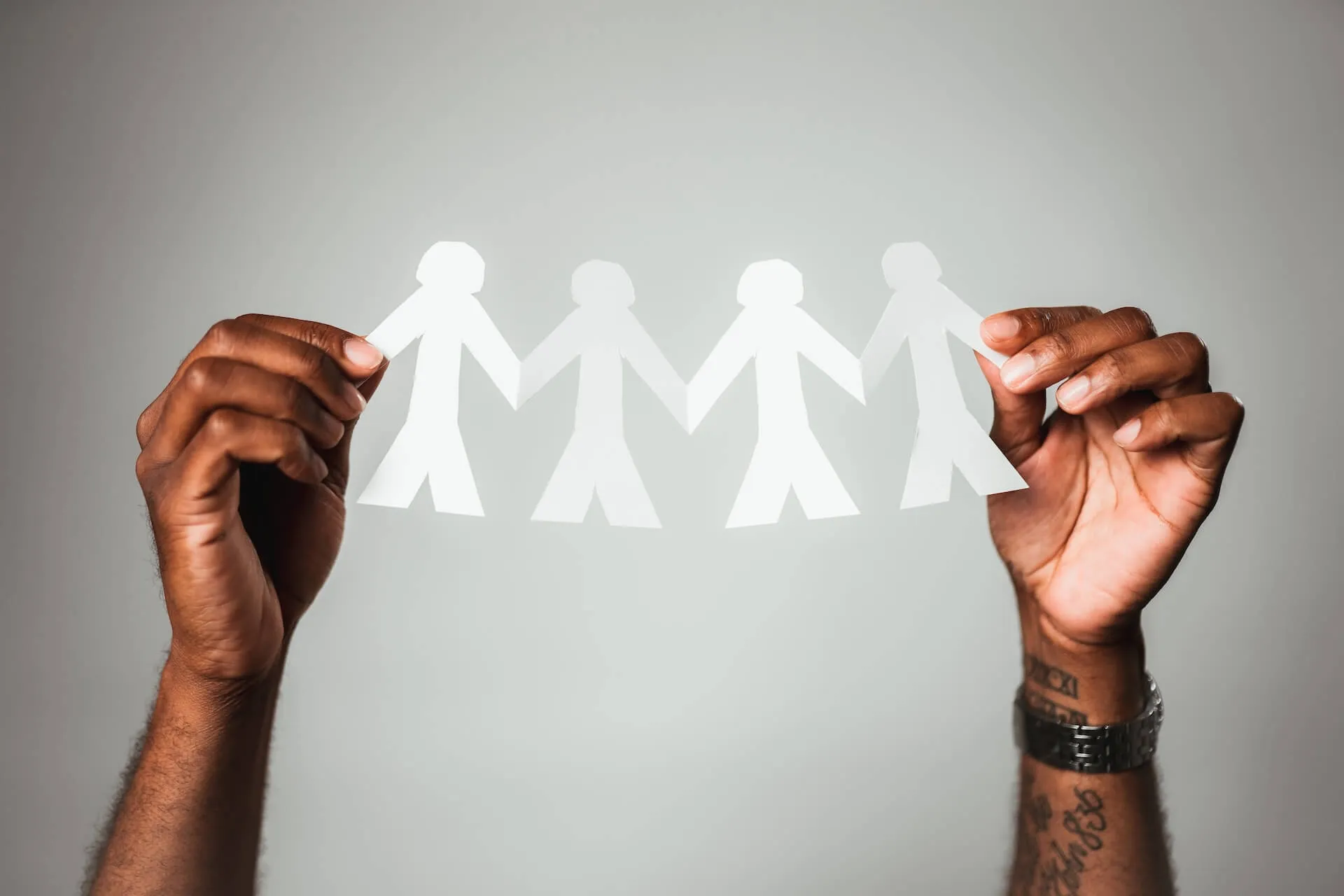 Close up of dark-skinned hands holding a white paper cutout of four linked human figures symbolizing solidarity