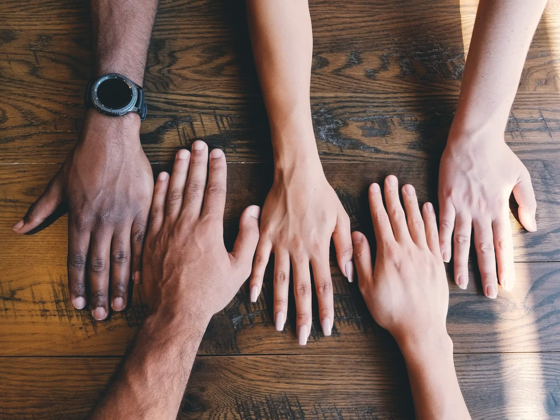 Five diverse hands palm down side by side on a wooden tabletop symbolizing unity and social justice