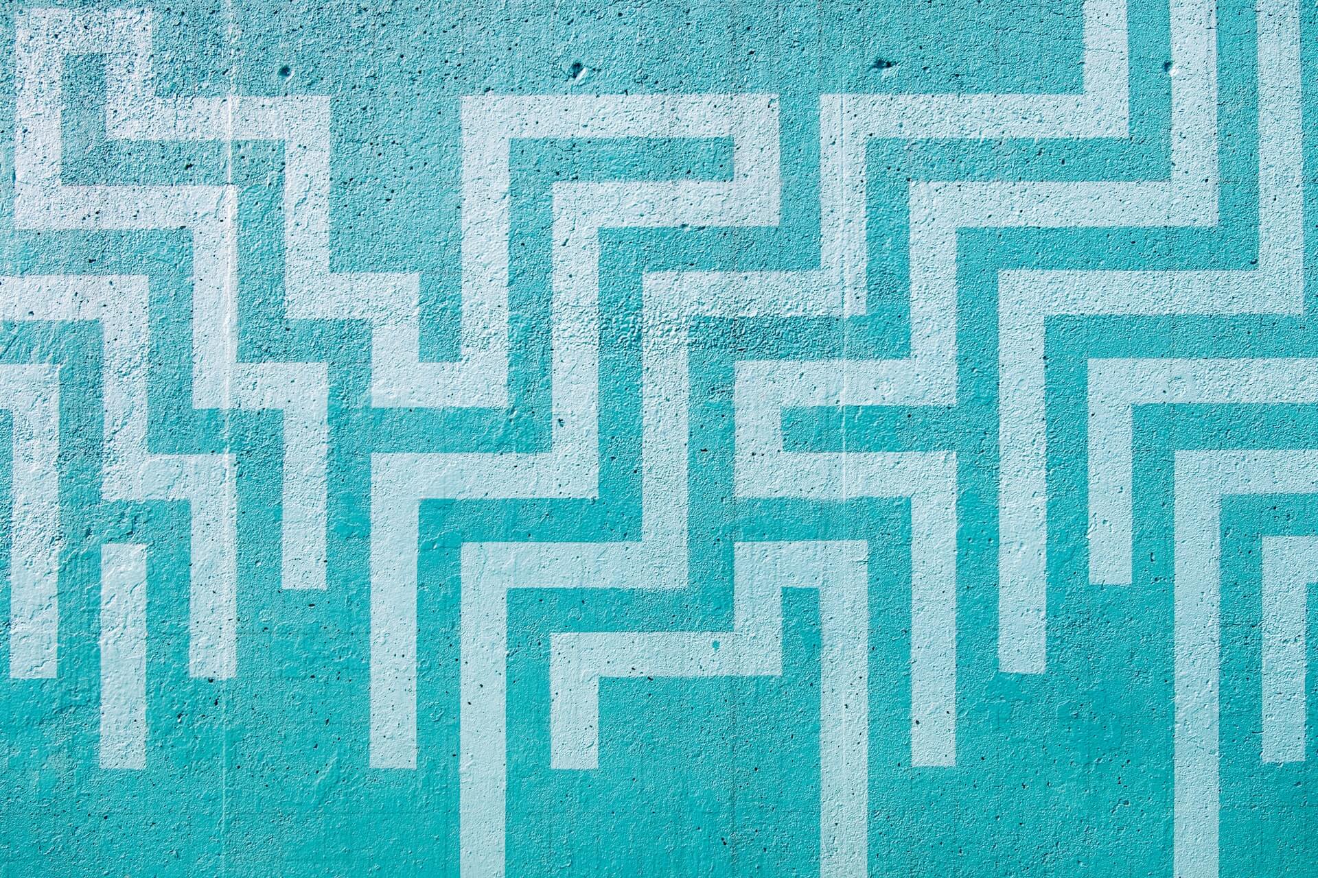 turquoise painted concrete surface covered in interlocking white right-angled pathways forming a stylized maze design