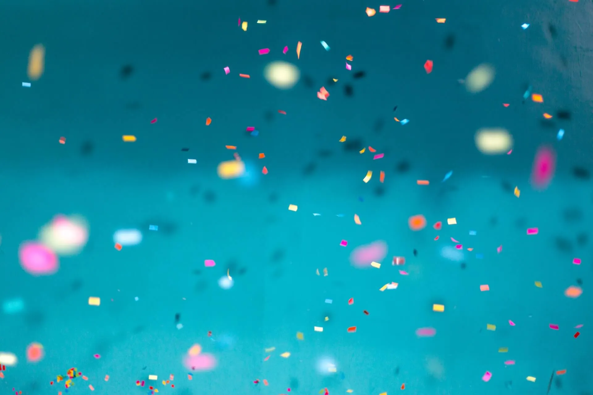 shower of small multicolor confetti pieces scattered across teal backdrop