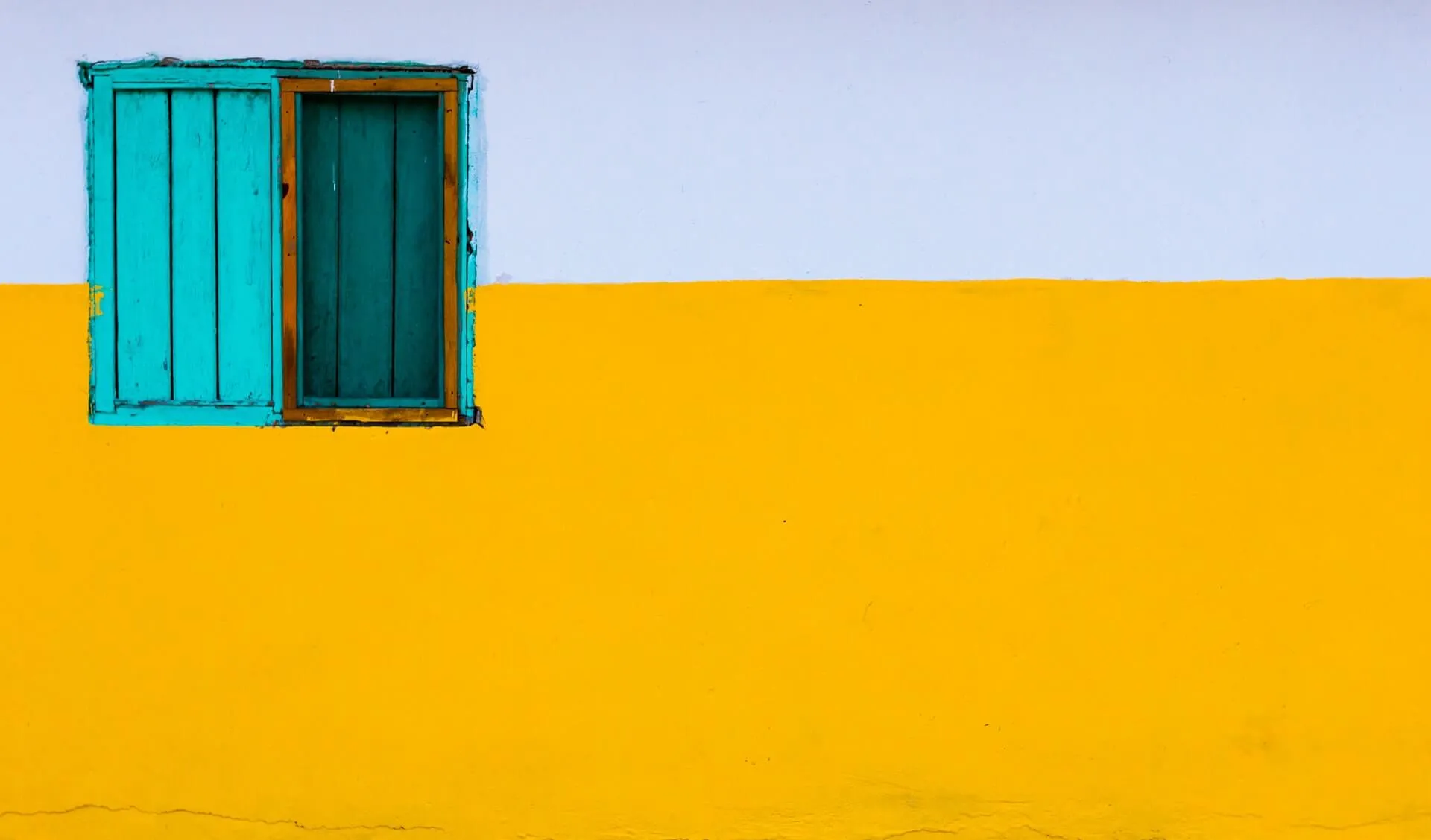exterior wall painted white on top and yellow on bottom with a turquoise wooden shutter window on the left
