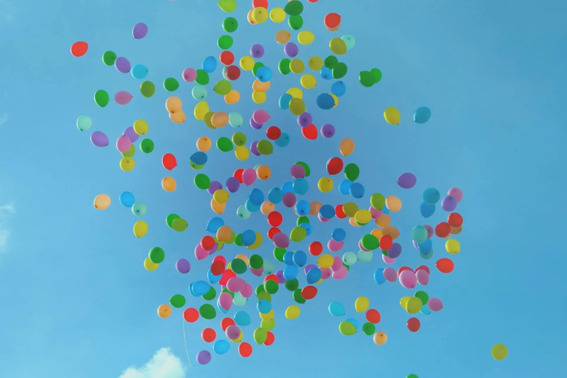 a large cluster of colorful balloons rising upward into a bright blue sky