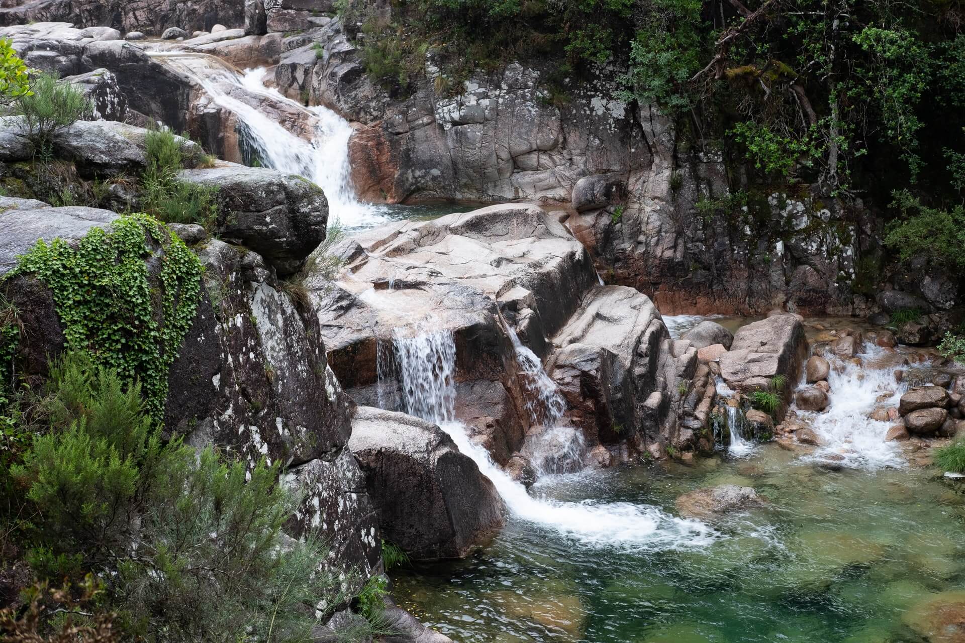 Cascading waterfall over smooth granite rocks into a clear emerald pool surrounded by lush green vegetation