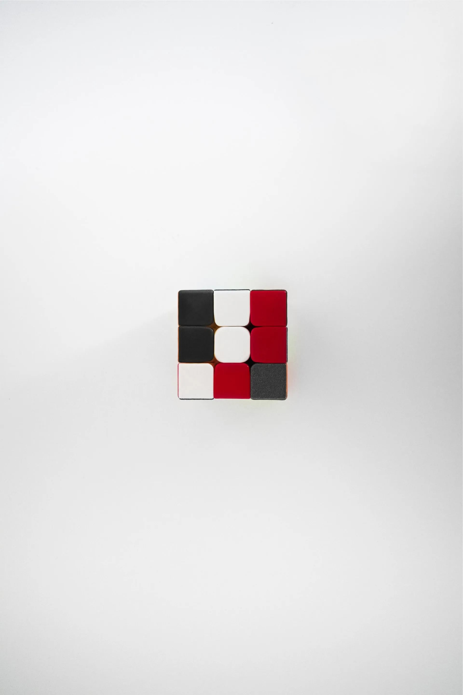 top down view of small 3x3 puzzle cube centered on white surface with red black and white colored stickers