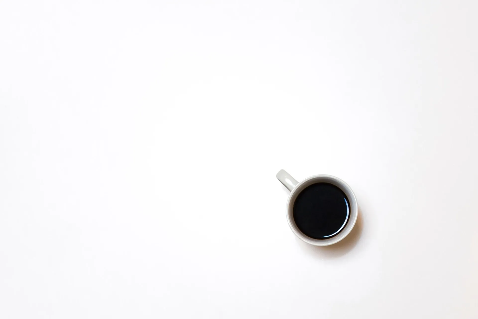 Top-down shot of a white coffee cup containing black coffee placed against a plain white background