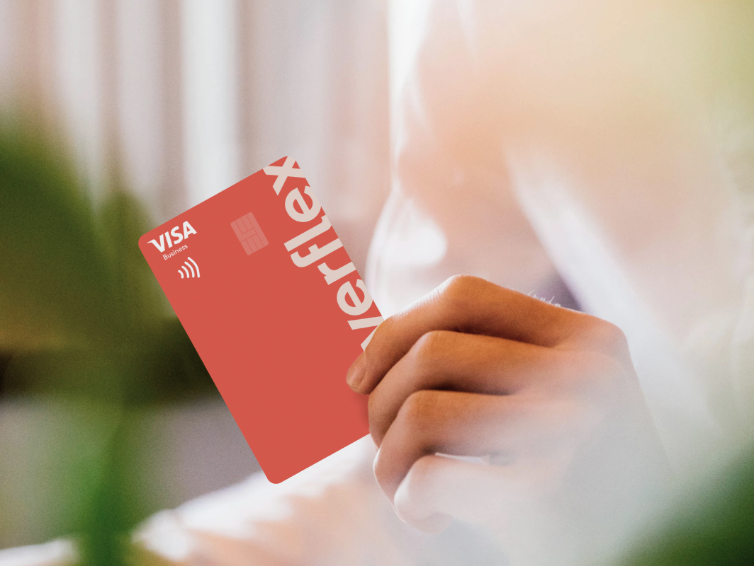Closeup of a hand gripping a red Coverflex Visa business card showing the chip and contactless logo in warm, soft-focused lighting