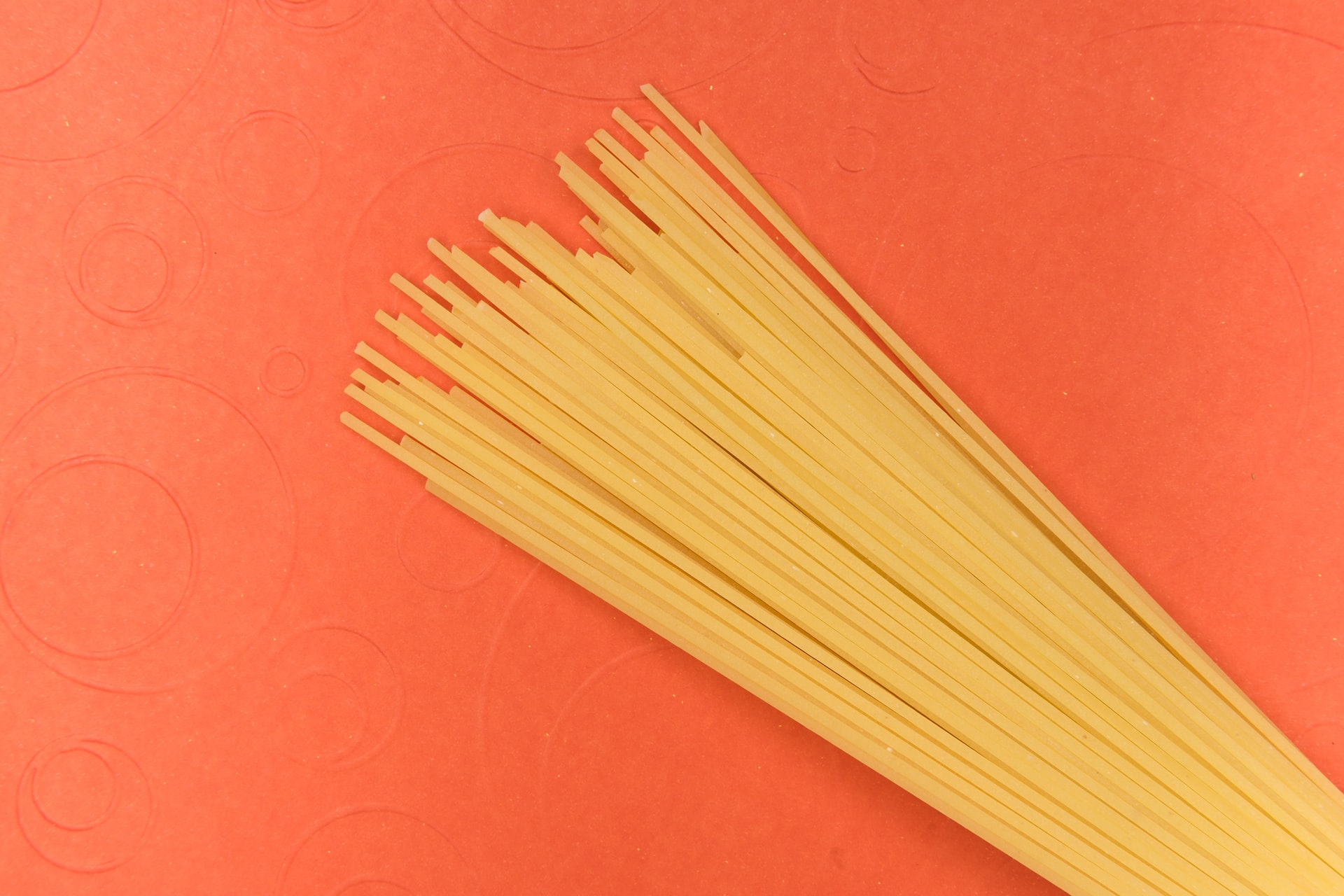 overhead view of uncooked spaghetti fanned out on a textured red background with circular embossing patterns