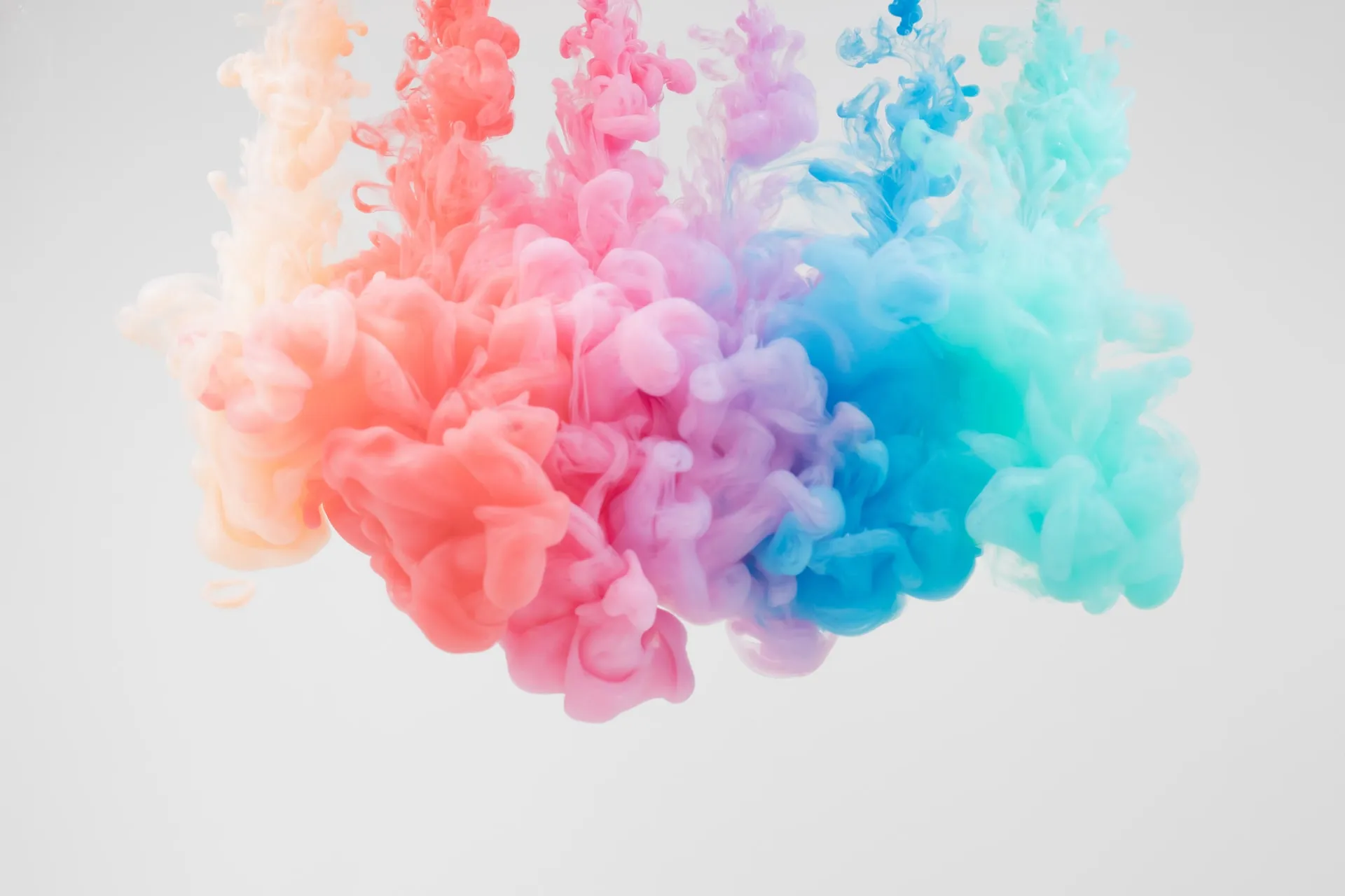 swirling clouds of colored ink in water blending coral, pink, lavender, blue and turquoise on a white background