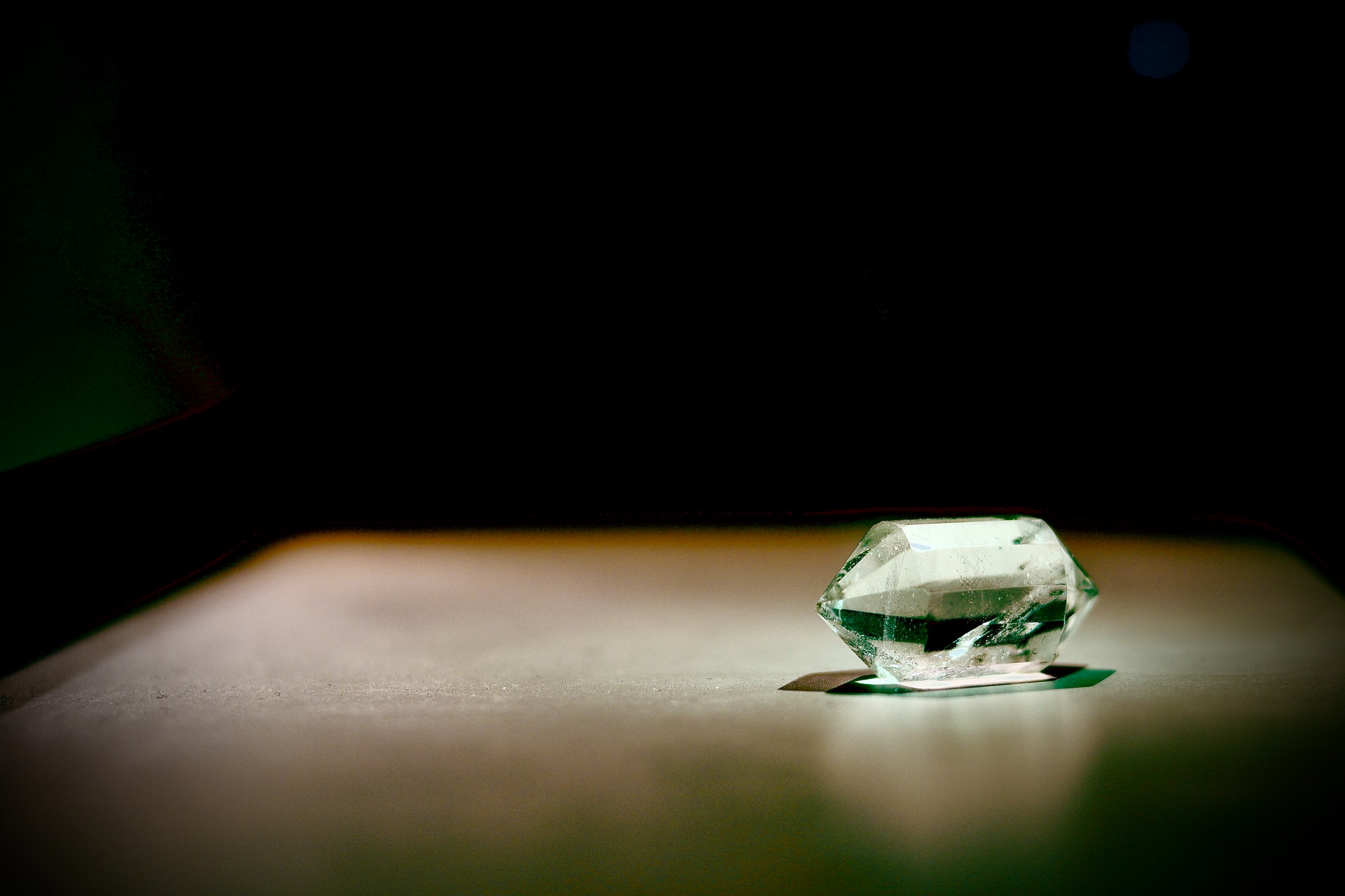 Transparent double-terminated quartz prism illuminated by green light on a smooth surface against a dark background