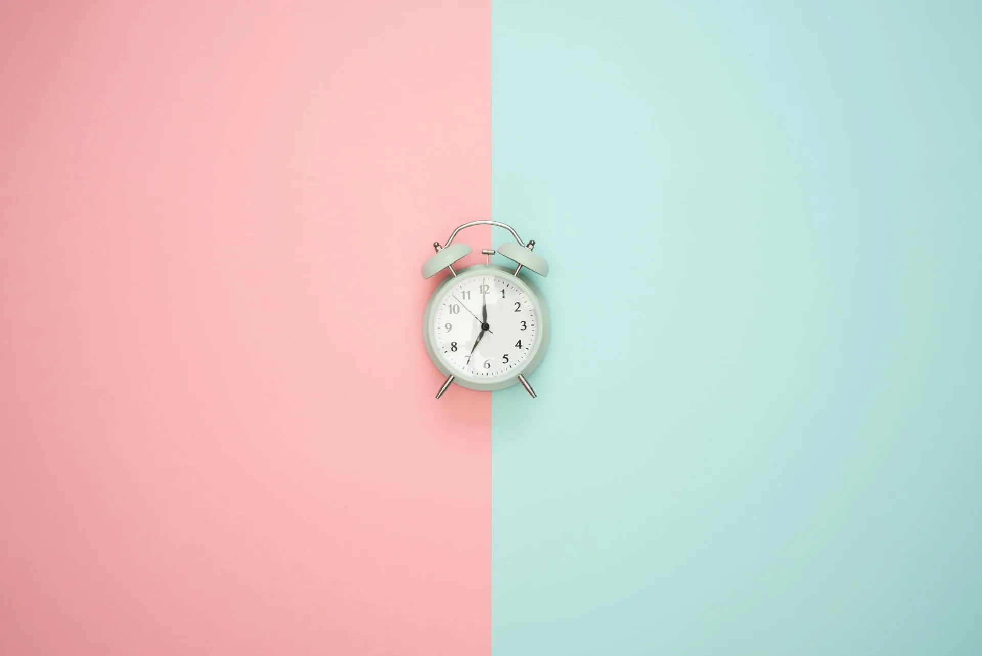 Mint green twin bell alarm clock centered on a split pastel background with pink on the left and mint green on the right