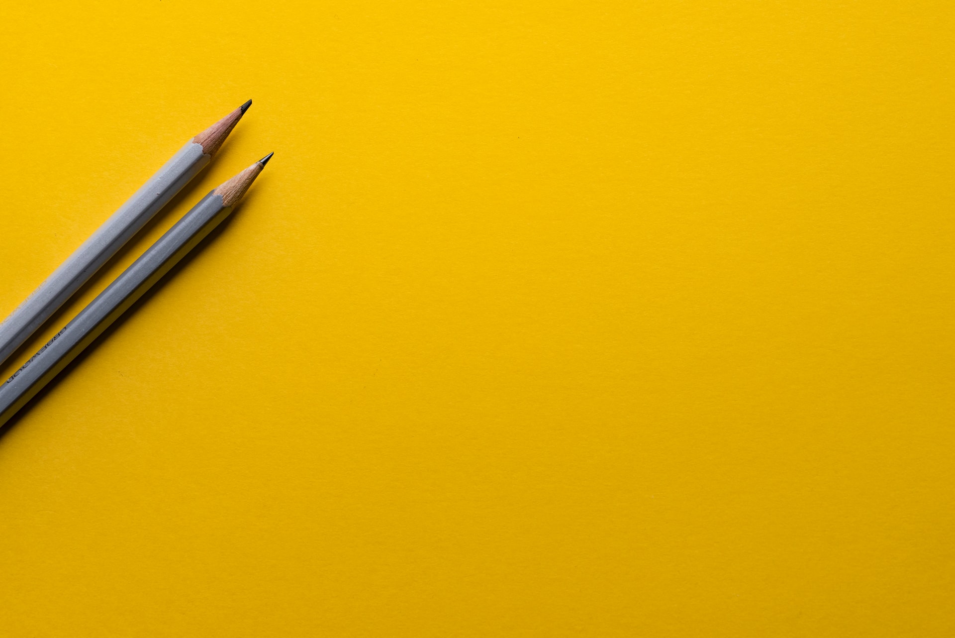 two sharpened grey wooden pencils placed diagonally on a solid yellow surface