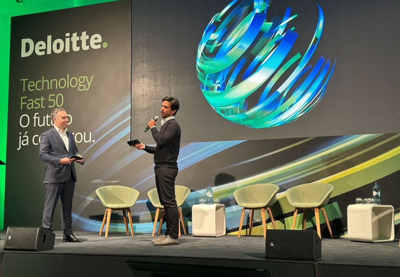 Hombre de pie en escenario con fondo de cartel Deloitte Technology Fast 50