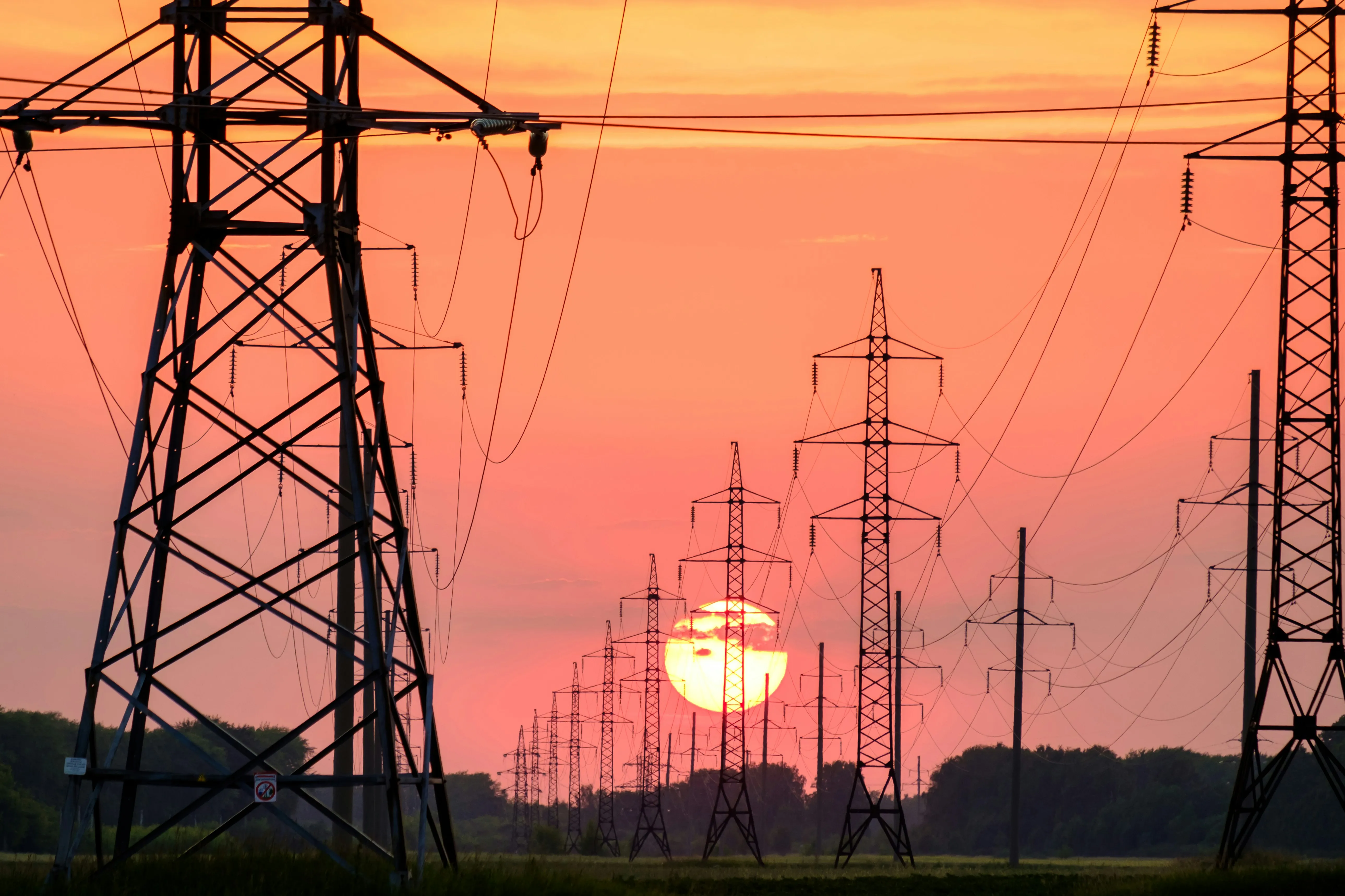 Lineas de torres de energia electrica al atardecer con sol rojizo en el horizonte y cables suspendidos sugiriendo corte de suministro