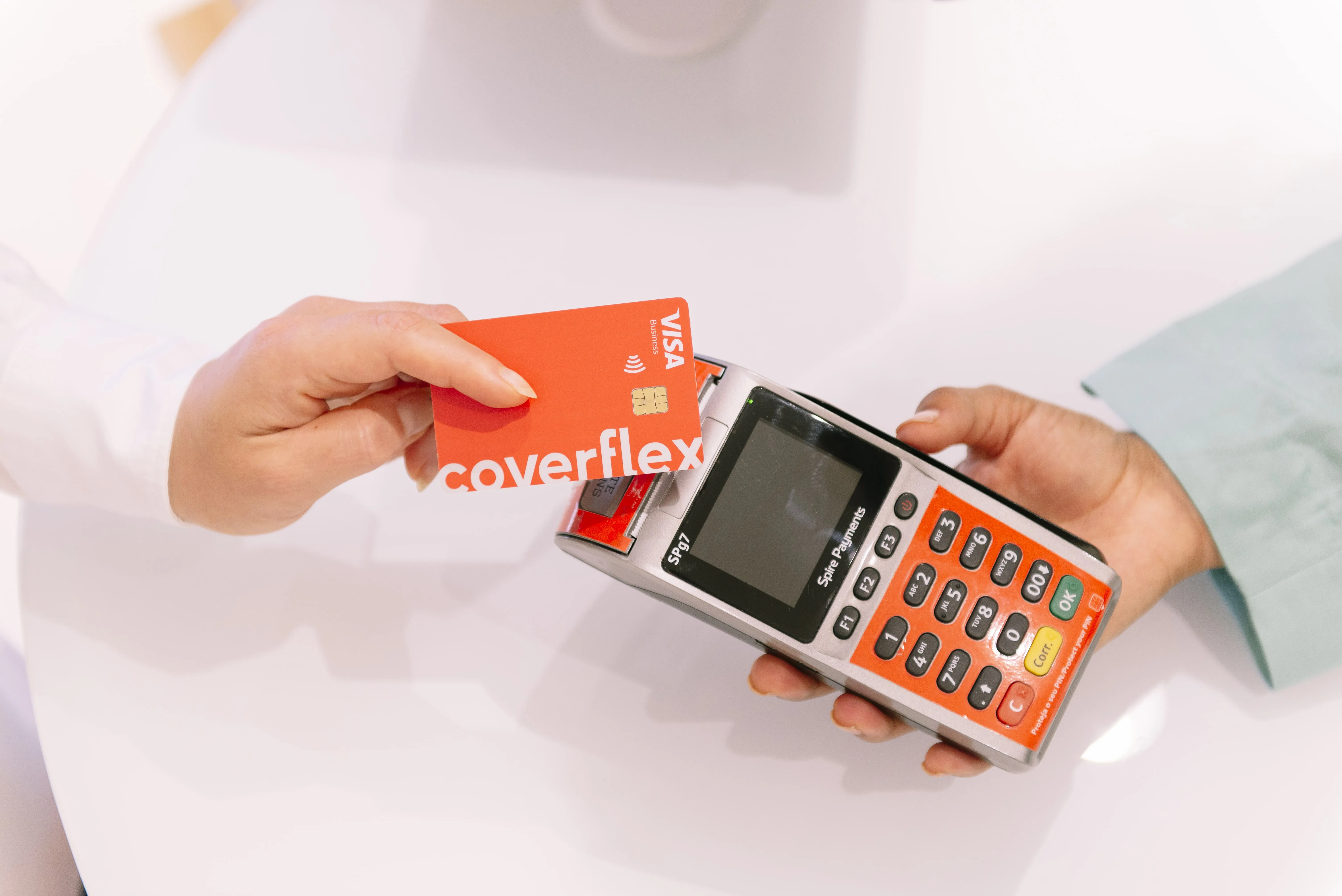 primer plano de dos manos una sosteniendo tarjeta Visa coverflex roja y otra un terminal de pago rojo realizando transacción sin contacto